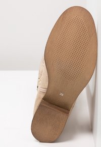 Beżowe buty z teksturowaną gumową podeszwą, dyskretnym wytłaczanym wzorem i drewnianym obcasem. Rozmiar 36 oznaczony na spodzie; widoczny szczegół zamka błyskawicznego z boku.