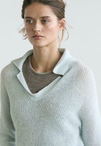 Light blue knit sweater with a chunky texture, featuring a deep V-neck and a contrasting gray inner layer. Soft and relaxed fit.
