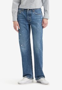 Vaqueros de denim azul claro con corte recto, que presentan detalles de salpicaduras de pintura blanca, cinco bolsillos y dobladillos deshilachados.