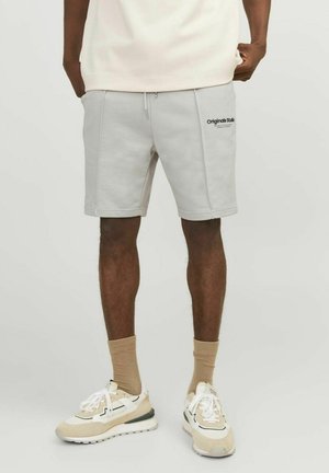 Pantalones cortos de color gris claro en una tela suave, con una cinturilla ajustable y bolsillos laterales. Un pequeño logo negro está impreso en el muslo izquierdo.