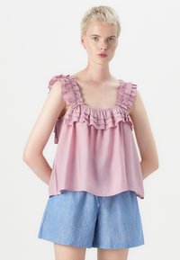 Roze mouwloze top met volants op de schouderbanden, losse pasvorm en lichtgewicht stof. Gecombineerd met blauw-wit gestreepte shorts.