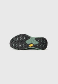 Semelle Vibram avec un revêtement en caoutchouc noir et des accents verts, texturée pour l'adhérence, et un logo jaune près de la zone du talon.