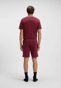Mörkröd träningssats bestående av en kortärmad topp och shorts. Mjukt tyg med elastisk midja. Bärs med svarta strumpor vid anklarna.