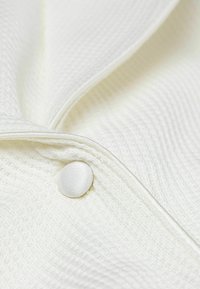 Witte textuurstof met een diagonaal patroon, voorzien van een gladde, ronde knop en een rits aan één kant. Subtiele glans.