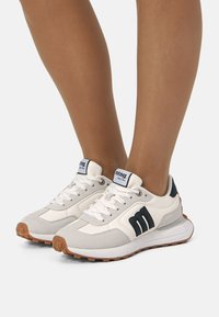 Sportliche Sneakers mit einem weißen und grauen Design, aus Wildleder und synthetischen Materialien, mit marineblauen Akzenten und einer dicken, strukturierten Gummisohle.
