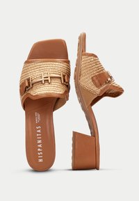 Sandales à glisser beiges avec une tige tissée en paille, des accents en cuir et un petit talon bloc. Comprend des détails de double boucle et une semelle texturée.