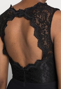 Svart klänning med en spetsbakgrund med scallopkanter och en djup skärning, som kontrasterar med ett slätt tyg vid midjan och kjolen.