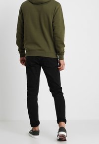 Olivgrön hoodie med känguruficka, parat med svarta slim-fit jeans. Svartvita sneakers med ett mönstrat sula.
