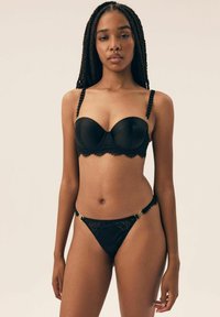 Black lingerie set featuring a padded balconette bra with lace trim and contrast ruffle straps, paired with a lace thong with gold hardware accents.