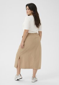 Fustă midi bej, cu slit lateral, talie elastică și textură netedă, asortată cu un top alb aderent și adidași gri.