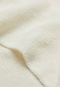 Tissu texturé de couleur crème avec un motif tissé, présentant une surface douce, légèrement surélevée et des plis délicats.