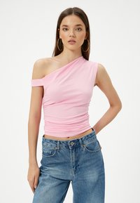 Top rosa, elástico, de un solo hombro con detalles fruncidos. Combinado con unos vaqueros de mezclilla azul claro, de cintura alta. Diseño simple y ajustado.