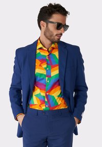 Blauw pak met een levendige, geometrische gestreepte shirt in geel, groen en paars. Zonnebril accentueert de look. Op maat gemaakt fit.