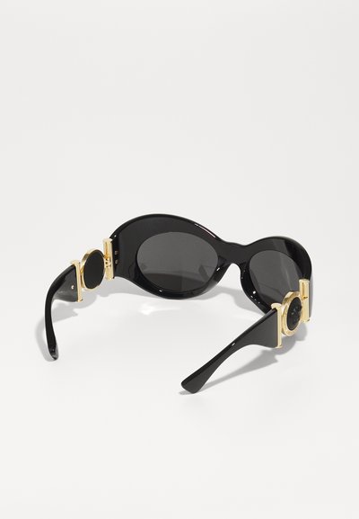 Lunettes de soleil ovales noires avec verres sombres. Fini brillant, dotées d'accents en métal doré sur les côtés. Design élégant et contemporain.