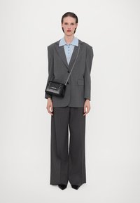 Blazer overdimensionato grigio a righe sottili su camicia azzurra con colletto, abbinato a pantaloni grigi a gamba larga e una piccola borsa nera con borchie.