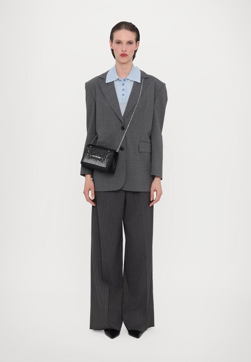 Blazer overdimensionato grigio a righe sottili su camicia azzurra con colletto, abbinato a pantaloni grigi a gamba larga e una piccola borsa nera con borchie.