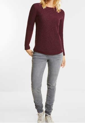 Pull en maille bordeaux à manches longues avec un motif texturé, associé à un jean gris slim et des baskets blanches. Design simple, look décontracté.