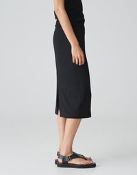 Schwarze Midikleider mit strukturiertem Stoff, seitlichem Schlitz und tailliertem Schnitt. Kombiniert mit flachen schwarzen Sandalen mit Schnallen-Detail.