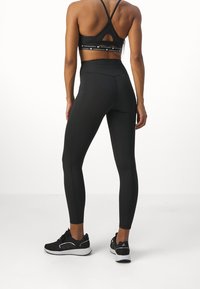 Czarny biustonosz sportowy z cienkimi ramiączkami i wycięciem, w zestawie z czarnymi legginsami o wysokim stanie. Oba elementy mają gładką fakturę i brak widocznych wzorów.
