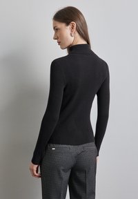 Maglione dolcevita nero a coste con maniche lunghe, design aderente, tessuto testurizzato e finitura liscia, abbinato a pantaloni neri con motivo.
