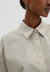 Beige striped shirt with a classic collar, featuring thin blue stripes, button front closure, and smooth fabric texture.