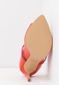 Chaussure à talon haut rouge avec un bout pointu et un design élégant, présentant une tige en cuir lisse et un talon aiguille fin. Semelle beige clair.