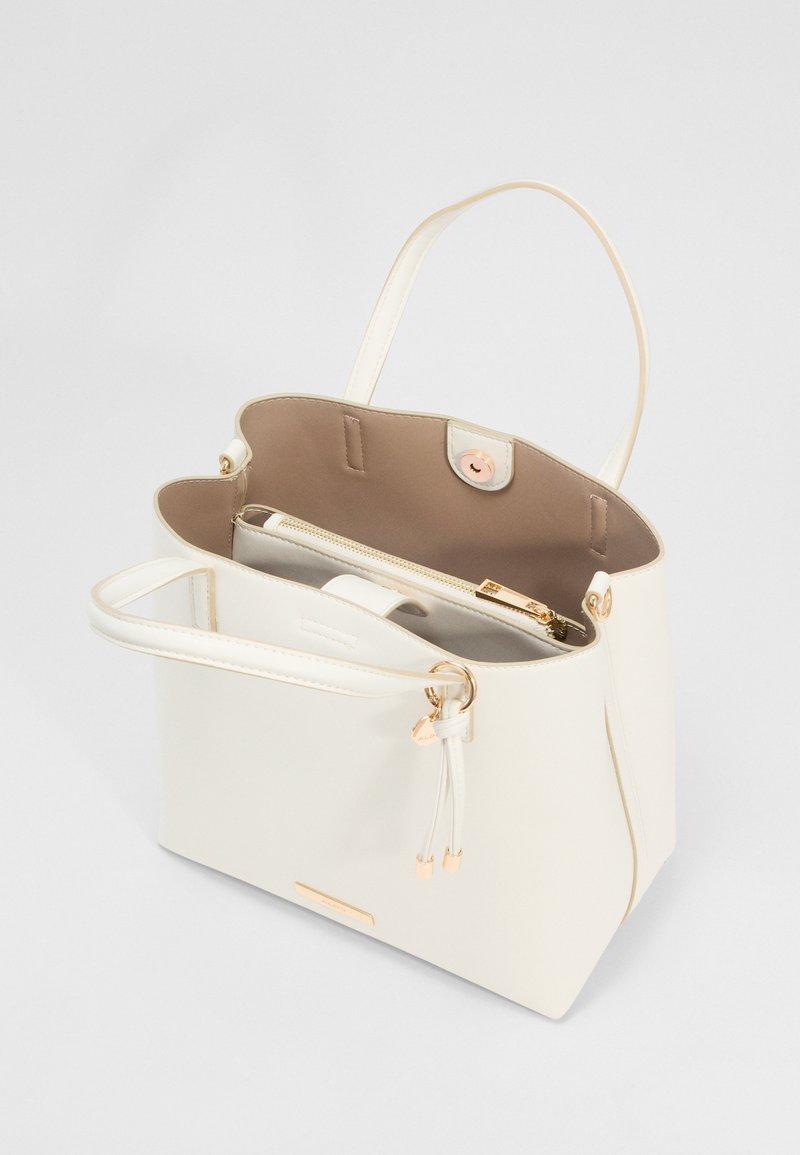 Sac fourre-tout couleur crème avec double poignées, une poche intérieure zippée, des accents dorés et une fermeture à pression magnétique, présenté ouvert sur un fond blanc.
