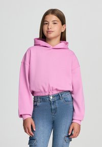 Felpa cropped rosa con cappuccio regolabile e maniche lunghe, abbinata a jeans azzurri chiari con tasche e vita aderente.