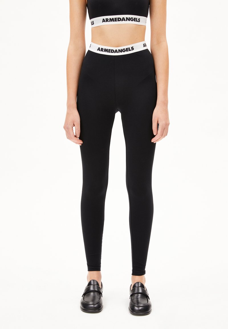 Zwarte legging van rekbaar materiaal, met een hoge tailleband waarop het "ARMEDANGELS" logo in het wit staat. Gladde textuur, slim fit ontwerp.