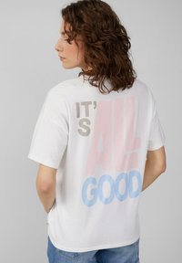 T-shirt en coton blanc à manches courtes, arborant un texte multicolore au dos : "C'EST TOUT BIEN" en rose et bleu. Coupe décontractée.