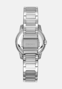 Orologio in acciaio inossidabile argentato con finitura lucida e opaca, caratterizzato da una cassa rotonda, bracciale a maglie e un dettaglio incavato DKNY sul retro.
