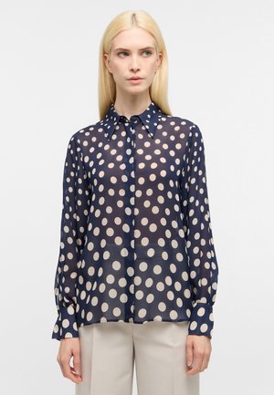 Blusa trasparente blu navy con grandi pois beige, colletto a bottoni, maniche lunghe e polsini con dettagli a pois abbinati.