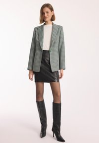 Zielono-biała marynarka w kratę z jednym guzikiem, zestawiona z czarną skórzaną mini spódnicą i czarnymi do kolan, wysokimi, szpiczastymi botkami.