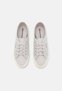 Jasnoszare trampki z materiału płóciennego, o okrągłym nosku, z sznurowaniem i białymi gumowymi podeszwami. Posiadają małe logo w kolorze czerwonym i niebieskim po boku.