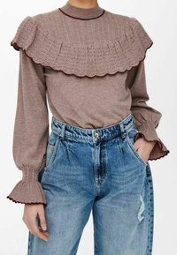 Haut en maille marron avec col volanté et détails aux poignets, associé à un jean en denim bleu taille haute avec un effet légèrement délavé.