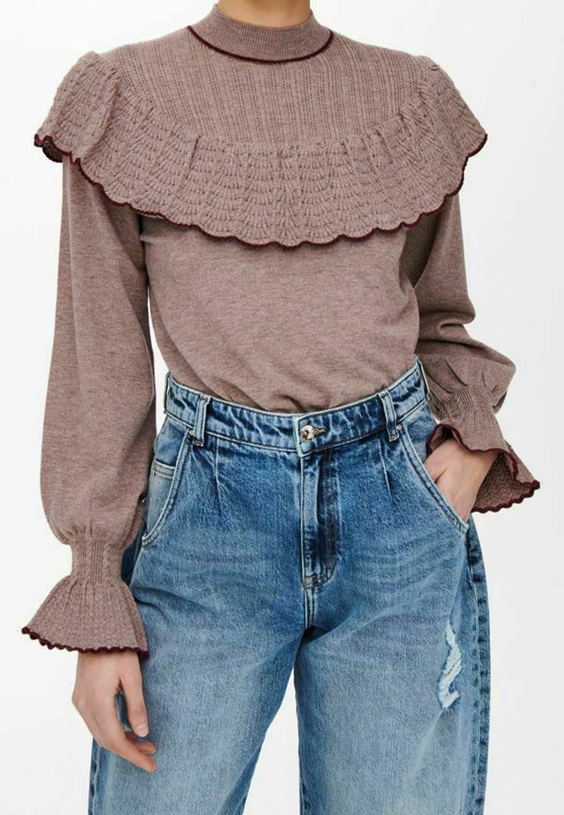 Haut en maille marron avec col volanté et détails aux poignets, associé à un jean en denim bleu taille haute avec un effet légèrement délavé.