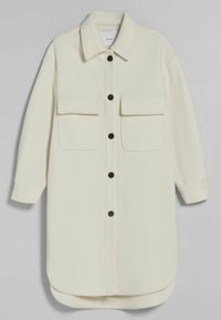 Giacca camicia oversize color crema con colletto, maniche lunghe, due tasche frontali e bottoni marrone scuro. Tessuto morbido e strutturato.