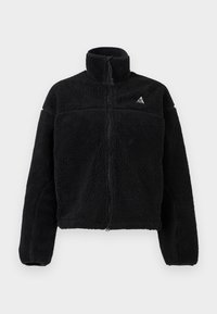 Jachetă neagră din fleece cu guler înalt, fermoar complet și model texturat. Prezintă un logo mic în partea stângă sus. Lungime scurtă.
