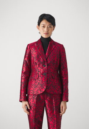 Completo sartoriale in raso rosso con motivo floreale nero, composto da un blazer a un petto, rever ailette e pantaloni coordinati. Texture liscia.