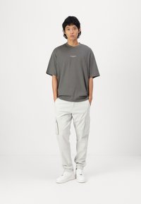 T-shirt gris ample avec un col rond, associé à un pantalon cargo gris clair avec des poches latérales et des baskets blanches.