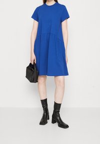 Blå kortärmad klänning med rund halsringning, samlad midja och lös passform. Matchad med svarta ankelboots och en liten svart väska.