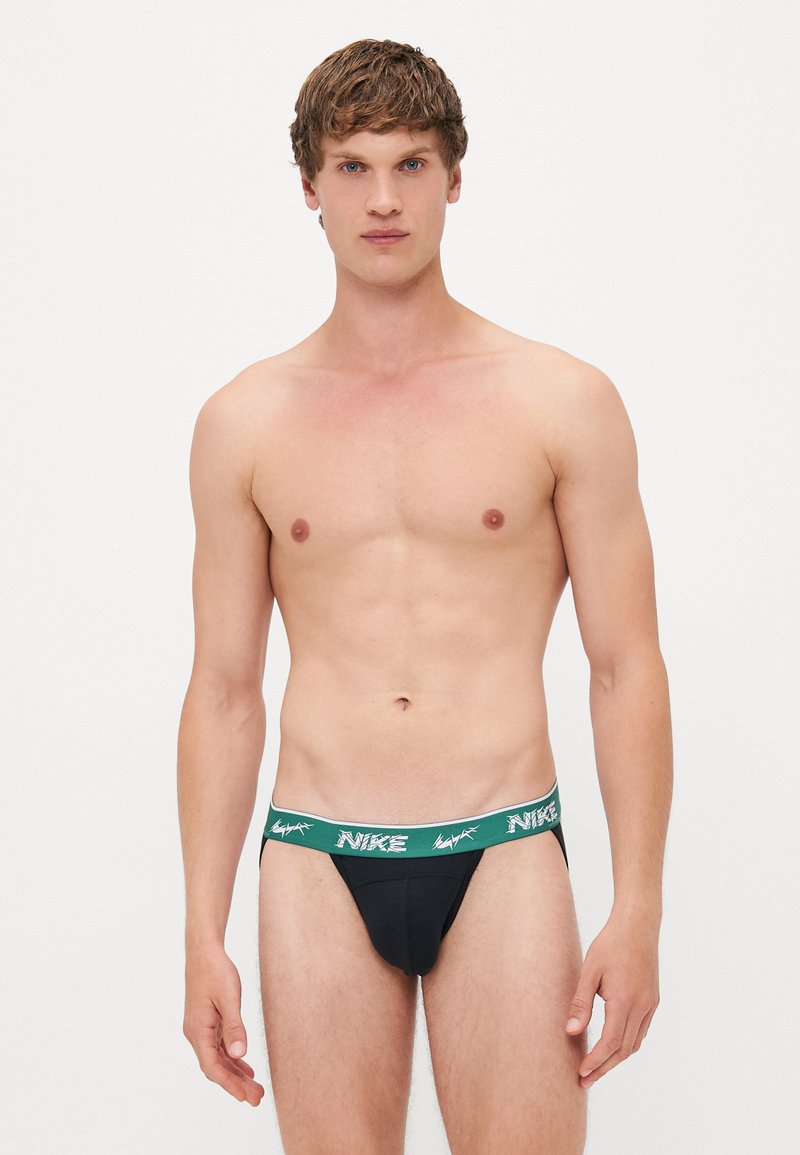 Schwarzer Nike-Tanga mit einem grün-weißen Markenbund, aus einem glatten, elastischen Stoff und einem figurbetonten Design.