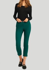 Černý top s dlouhým rukávem a tyrkysové kalhoty se slim fit střih. Kalhoty mají na spodním lemu boční štěrbiny. Černé loafery se zlatým řetízkovým detailem.