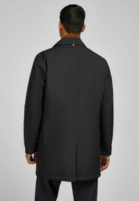 Zwarte jas met een gestructureerd ontwerp, voorzien van een bruine kraag en zichtbare naden aan de achterkant. Gemaakt van textuurstof.