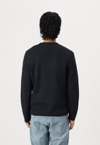 Donkerblauwe gebreide trui met een ronde hals, lange mouwen en een gestructureerde afwerking, gecombineerd met lichtblauwe denim jeans.
