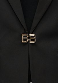 Blazer noir fermé par un fermoir doré entrelacé en forme de double "B" au centre devant.