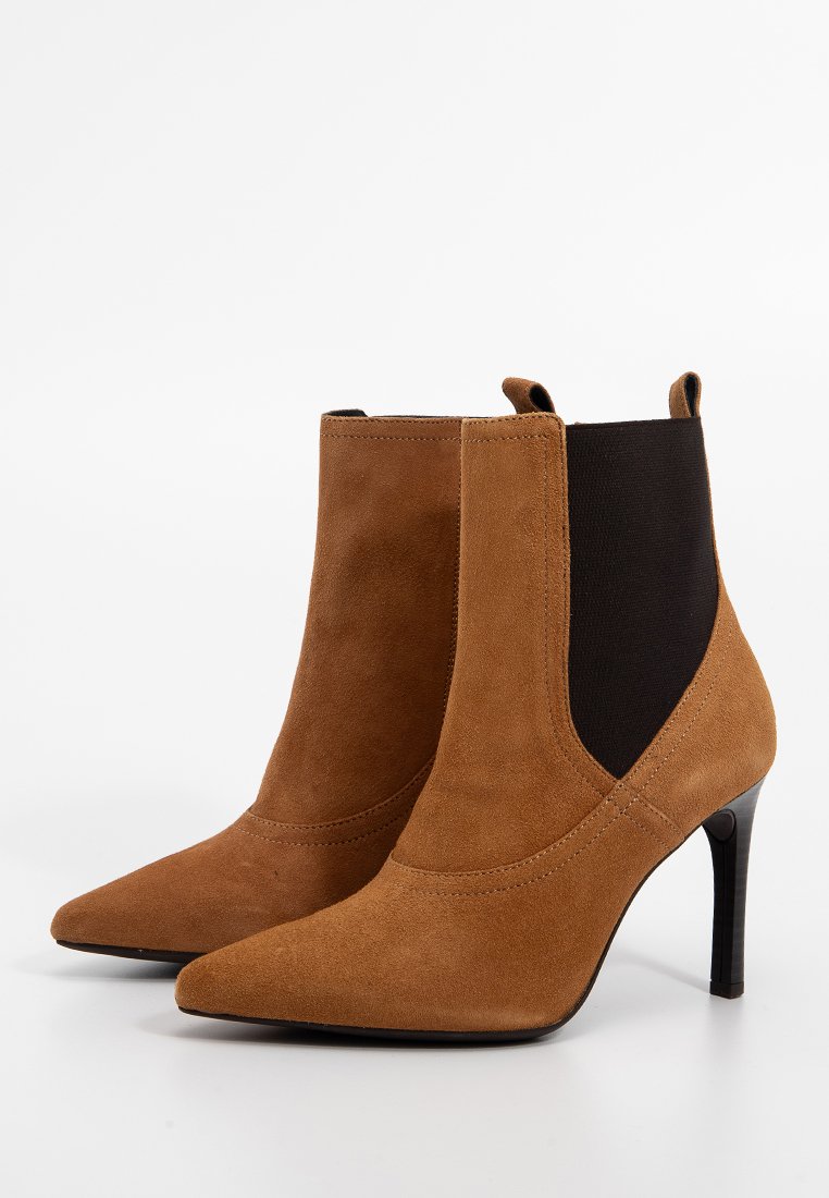 Stivali ankle in suede marrone con punta appuntita, pannelli laterali elastici neri e tacco a stiletto. Texture liscia con dettagli di cucitura minimi.