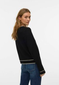 Must kampsun ümarate kaelusega ja kreemika ääristusega ääres ja varrukateotstes, kombineeritud siniste teksapükstega, mille lõige on lõdvestunud.