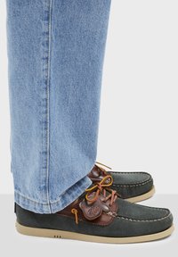 Zapatos de hombre en ante gris oscuro con detalles en piel marrón, suela beige y costura decorativa. Combinados con jeans de color azul claro.