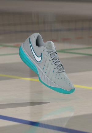 Grauer und türkisfarbener Nike Sportschuh mit weißem Swoosh, der über einem Hallensportplatzboden mit farbigen Linien schwebt.